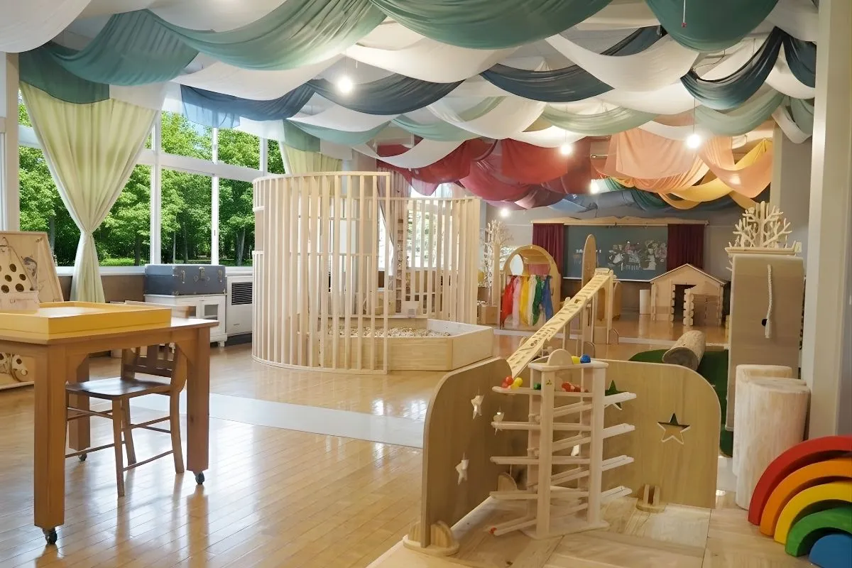 宮城県産材でできた里山エスクエラの明るい室内。木材のテーブルと椅子が並び、大きな窓からは緑が見える。