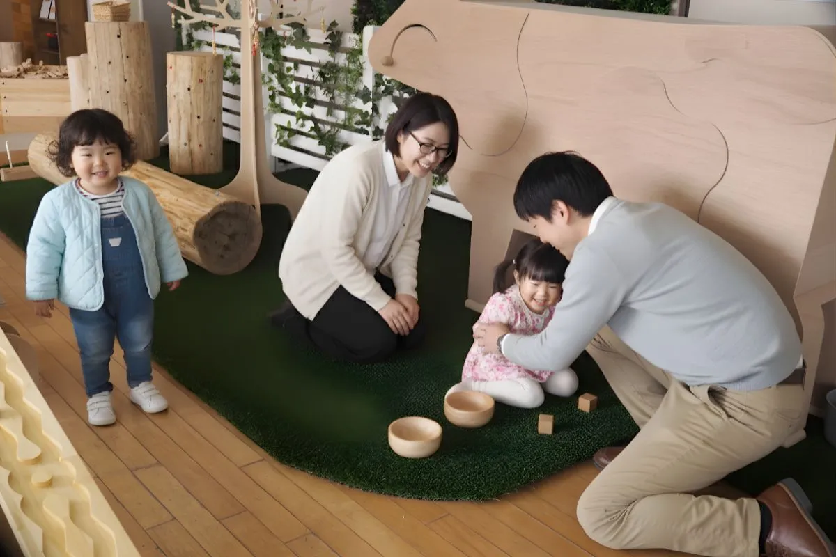 木育広場『里山エスクエラ』の木製牛さん（乳搾り体験ができる遊具）で、が親子が笑顔で遊んでいます。楽しそうにしている様子が伺え、温かい空間が伝わります。